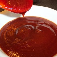 a spoon full of ketchup being drizzled on top of a white bowl