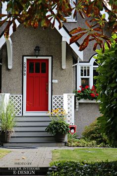 a red door sits in front of a gray house with white trim and flowers on the steps