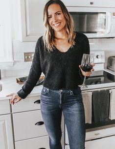 a woman standing in a kitchen holding a glass of wine