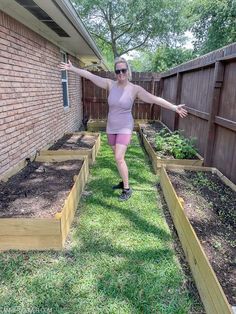 a woman in pink shorts and sunglasses standing next to a row of wooden raised garden beds