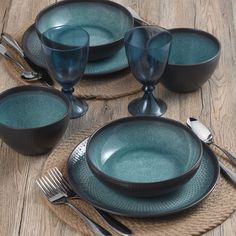 a place setting with blue dishes and silverware on a wooden tableclothed placemat