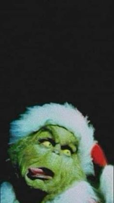 the grinch is wearing a santa hat and holding a cell phone to his ear