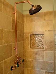 the shower head is mounted on the wall next to the tiled bathtub with copper faucet