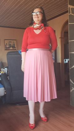 a woman in a red top and pink pleated skirt is posing for the camera