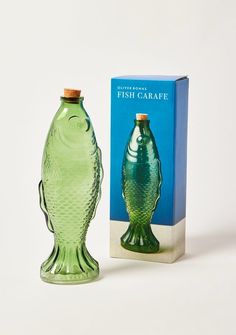 a green glass fish shaped bottle next to a box