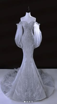 a white wedding dress with long sleeves and sheers on the shoulders, in front of a black background