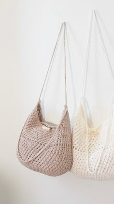 two crocheted purses hanging from hooks on a wall, one in white and the other in beige