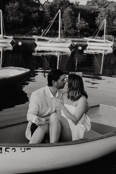 a man and woman are sitting in a boat on the water with sailboats in the background