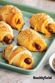 pigs in a blanket on a baking tray next to some spices and seasoning nearby