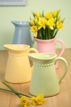 three vases with yellow flowers in them on a wooden table next to each other