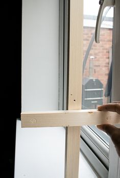 a person holding a piece of wood in front of a window