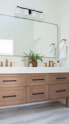 a bathroom vanity with two sinks and a large mirror above it, in front of a white tiled floor