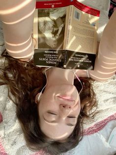 a woman laying on top of a bed with a book in her hand over her head