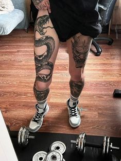 a man with tattoos on his legs standing in front of a barbell and dumbs