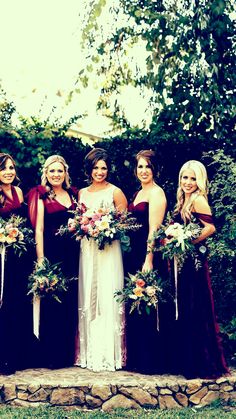 a group of women standing next to each other in front of a stone wall holding bouquets