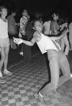 black and white photograph of people dancing on checkered floor in an open area with one person holding out his hand