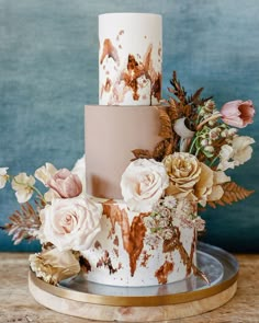 a three tiered cake decorated with flowers and leaves on a wooden table next to a blue wall