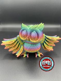 a colorful owl figurine sitting on top of a gray table next to a sticker