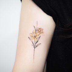 a small yellow flower tattoo on the left arm