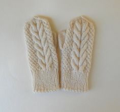 two white knitted mittens sitting on top of a white table next to each other