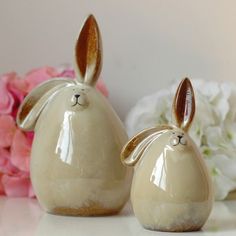 two ceramic rabbits sitting next to each other on a white table with flowers in the background