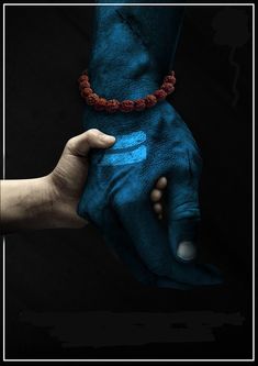 two hands are holding each other with blue paint on their palms and red beaded bracelets