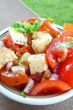 a white bowl filled with tomatoes, onions and tofu on top of a table