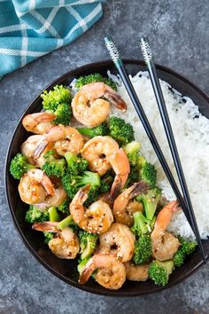 shrimp and broccoli stir fry with rice in a black bowl on a gray surface