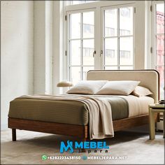 a bed sitting in front of a window next to a table with a lamp on it