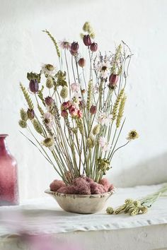 a white bowl filled with lots of flowers on top of a table next to a pink vase