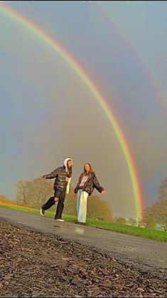 two people walking down a road with a rainbow in the background