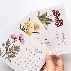 a person holding three calendars with flowers on them