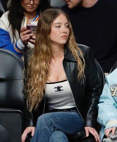 a woman with long hair sitting in the stands at a basketball game while looking at her cell phone