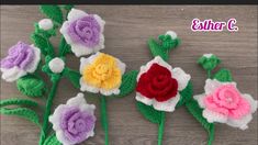 crocheted flowers with leaves and stems on a wooden surface, one is purple, the other is red