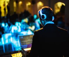 a man wearing headphones sitting in front of a laptop computer with glowing lights behind him