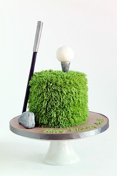 a green cake with a golf ball on top and a tee in the middle, sitting on a plate