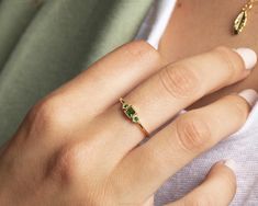 a close up of a person wearing a ring with green stones on the middle finger