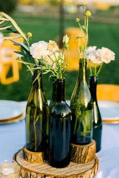 three bottles with flowers in them sitting on a wooden stand next to plates and glasses