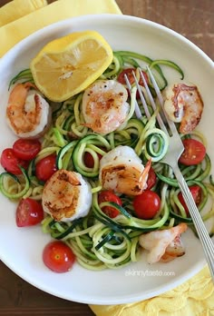 a white plate topped with shrimp and zucchini noodles next to a lemon wedge