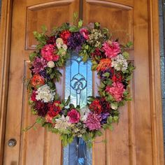 a wreath is hanging on the front door with flowers around it and a stained glass window in the background