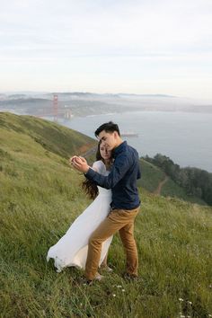 a man and woman are dancing in the grass on top of a hill near the ocean