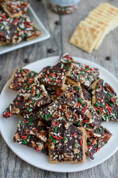 a white plate topped with chocolate covered pretzels and sprinkles next to crackers