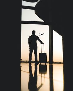 a man is standing in an airport with his luggage and looking at the plane flying overhead