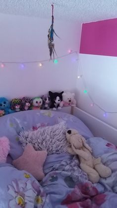 a bed with stuffed animals on it and lights strung from the ceiling above them in a bedroom