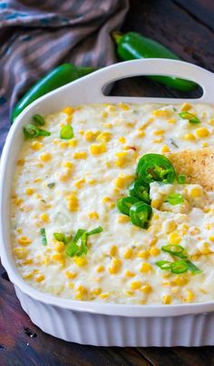 a white casserole dish with corn and green peppers in it on a wooden table