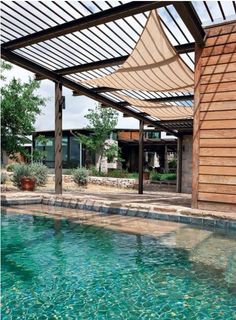 an outdoor swimming pool surrounded by wood and stone walls, with a pergolated roof over it