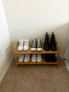 four pairs of shoes are lined up on a wooden shoe rack in the corner of a room