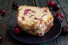 a piece of cake sitting on top of a black plate next to cherries and a fork