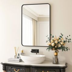 a bathroom with a sink, mirror and flowers on the counter top in front of it