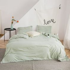 a bed with green sheets and pillows in a room next to a white wall that says love